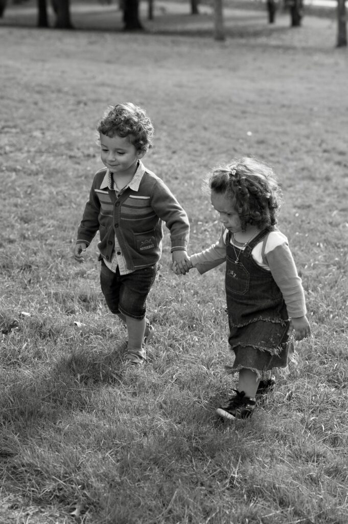 due bambini di circa 2 anni si tengono per mano mentre camminano sull'erba. rappresentano un piccolo grande amore